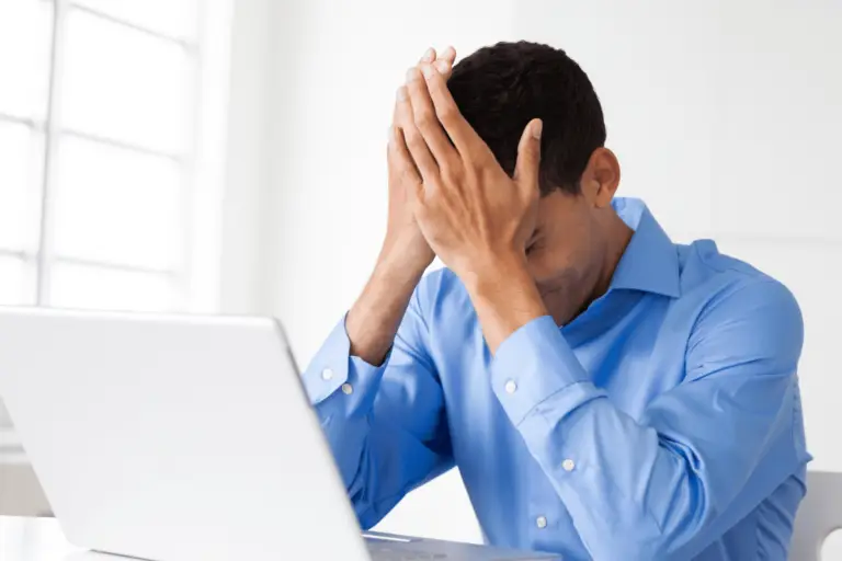 A man, sitting in front of a computer, has his head in his hands